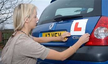 Woman putting learner plates on blue Renault Clio vehicle